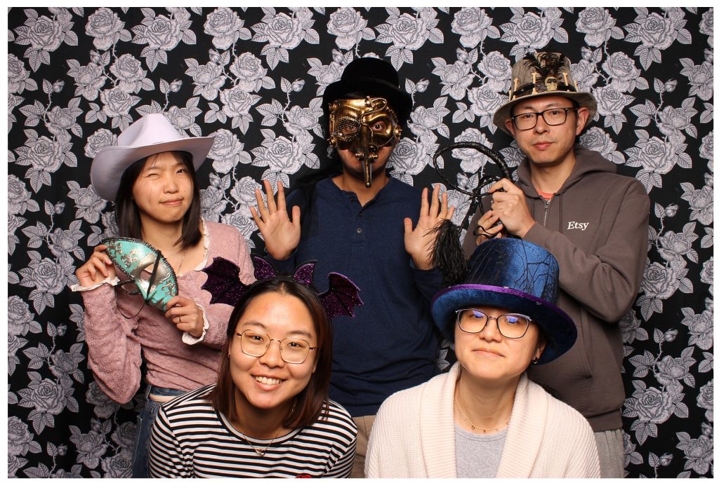 A group dressed in costume taking a photo in front of a Halloween Photo Booth.