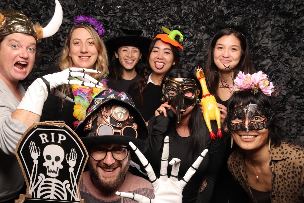 A group dressed in costume taking a photo in front of a Halloween Photo Booth.