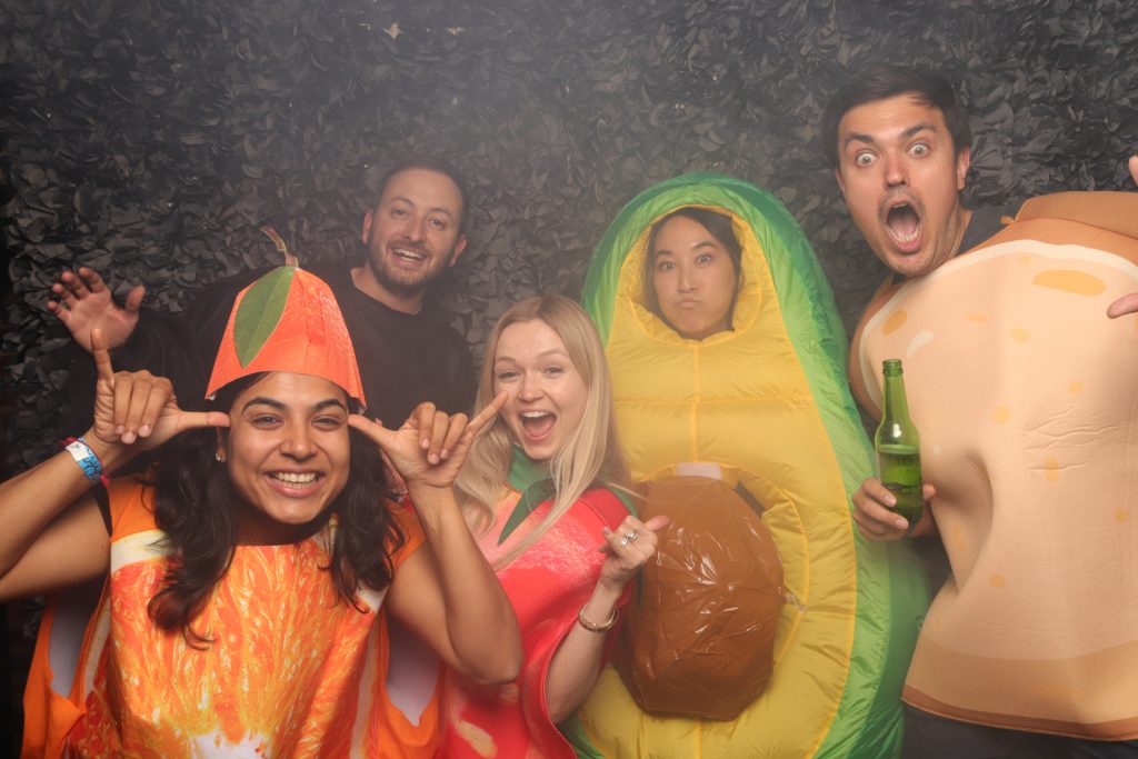 A group dressed in costume taking a photo in front of a Halloween Photo Booth with faux fog.