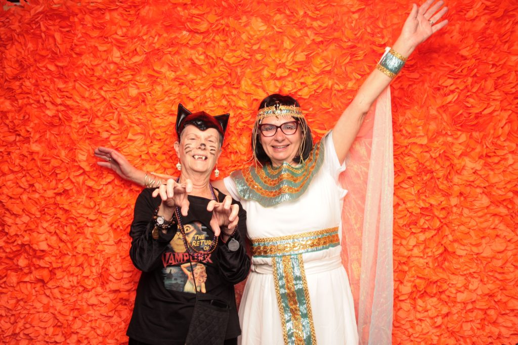 Two women dressed in costume taking a photo in front of a Halloween Photo Booth.