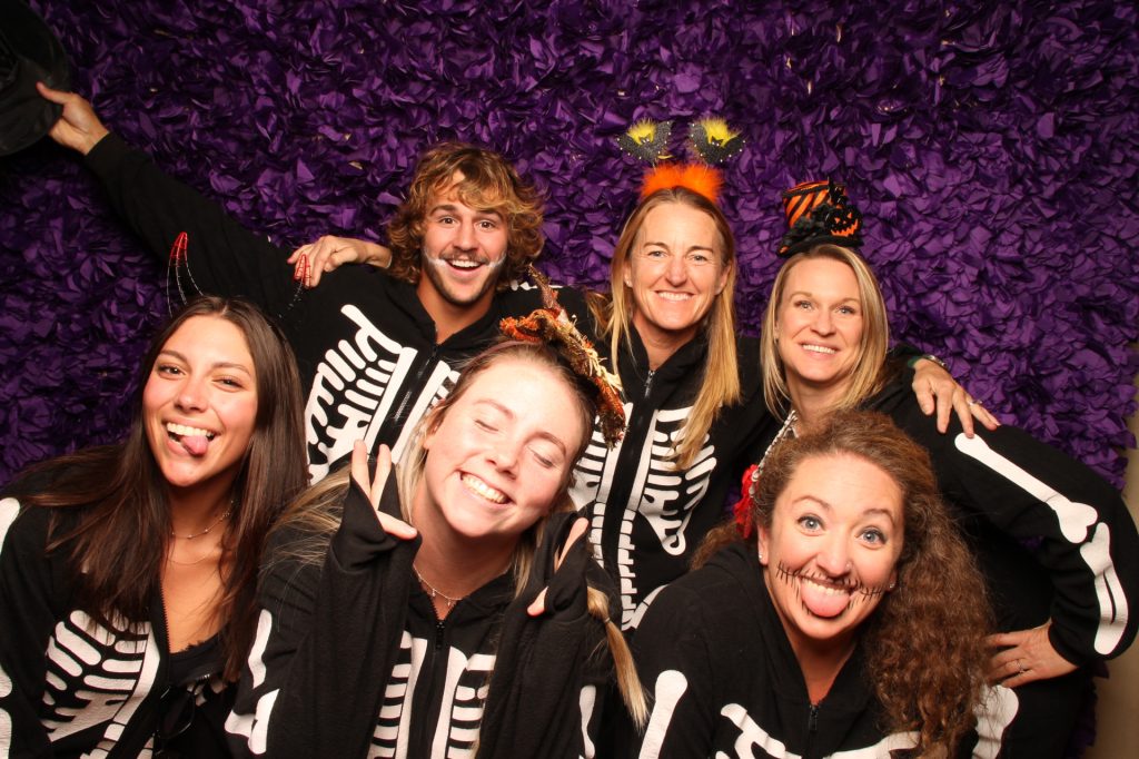 A group of people dressed in costume taking a photo in front of a Halloween Photo Booth.