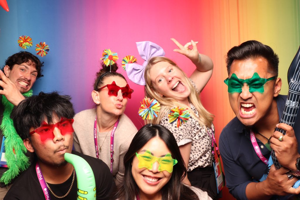 Group pose for a photo in front of a colorful backdrop in an open air photo booth.