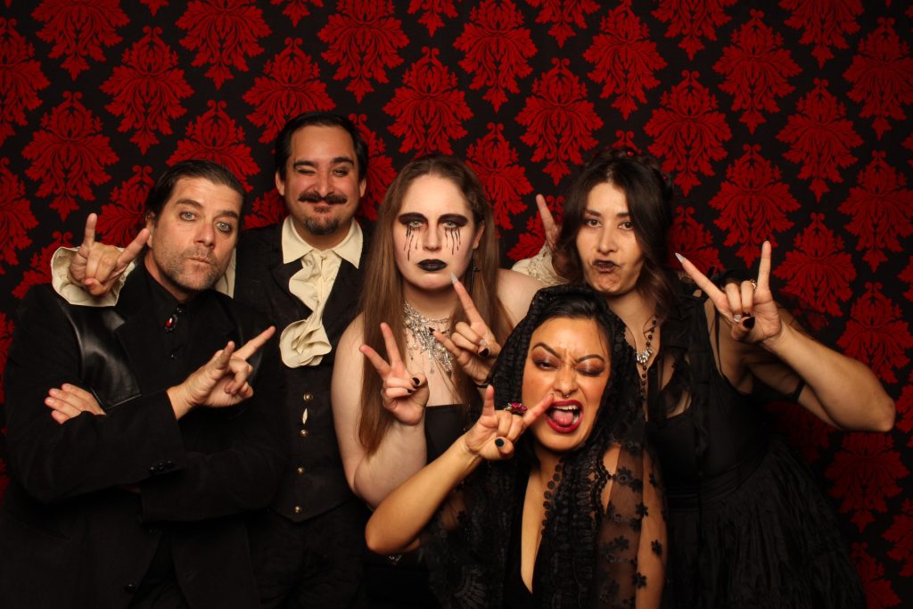 A group dressed in costume taking a photo in front of a Halloween Photo Booth.