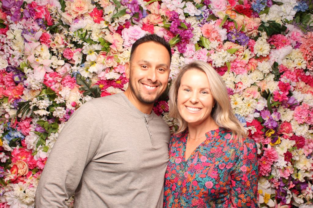 Man and woman posing for a photo in front of the Floral Wall for a Spring Photo Booth