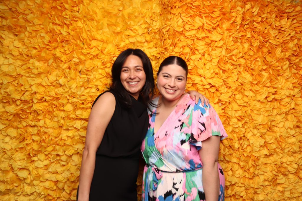 Two women pose for a photo in front of an open-air photo booth.