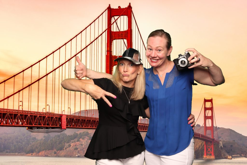 Two women pose for a photo in front of a greenscreen San Francisco Photo Booth.