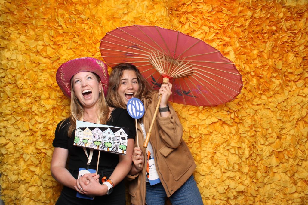 Two women pose for a photo in front of a spring open-air photo booth.
