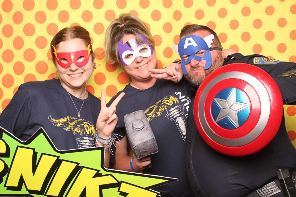 A group poses with for a photo booth with a superhero theme.