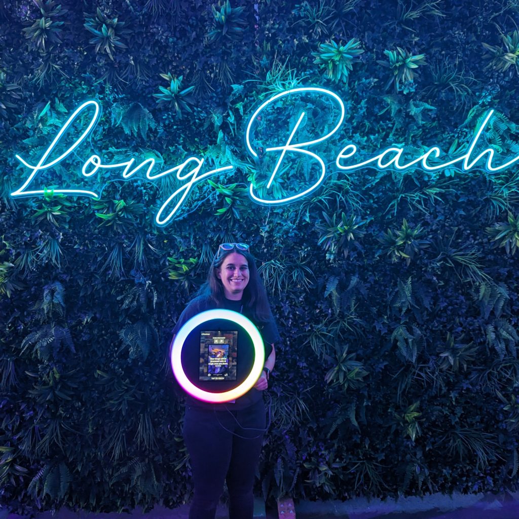 woman holding our roamer photobooth with plants and a neon sign behind her