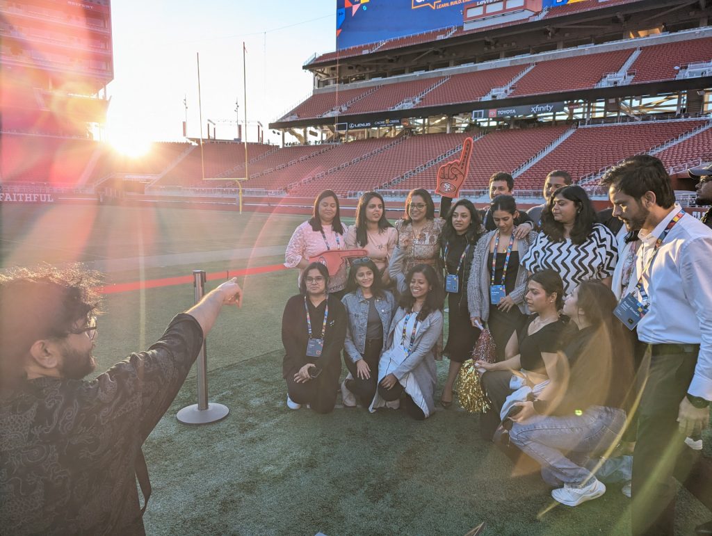 A man directing a photo shoot of a group of people standing inside Levi Stadium.