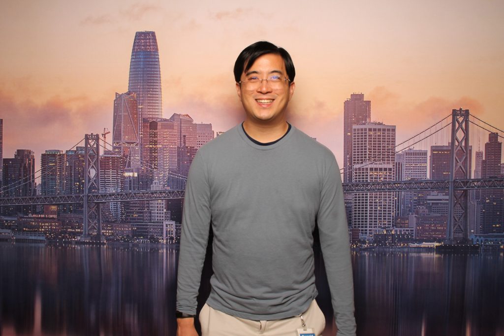 Guy stands for a photo in front of the San Francisco Sunset backdrop