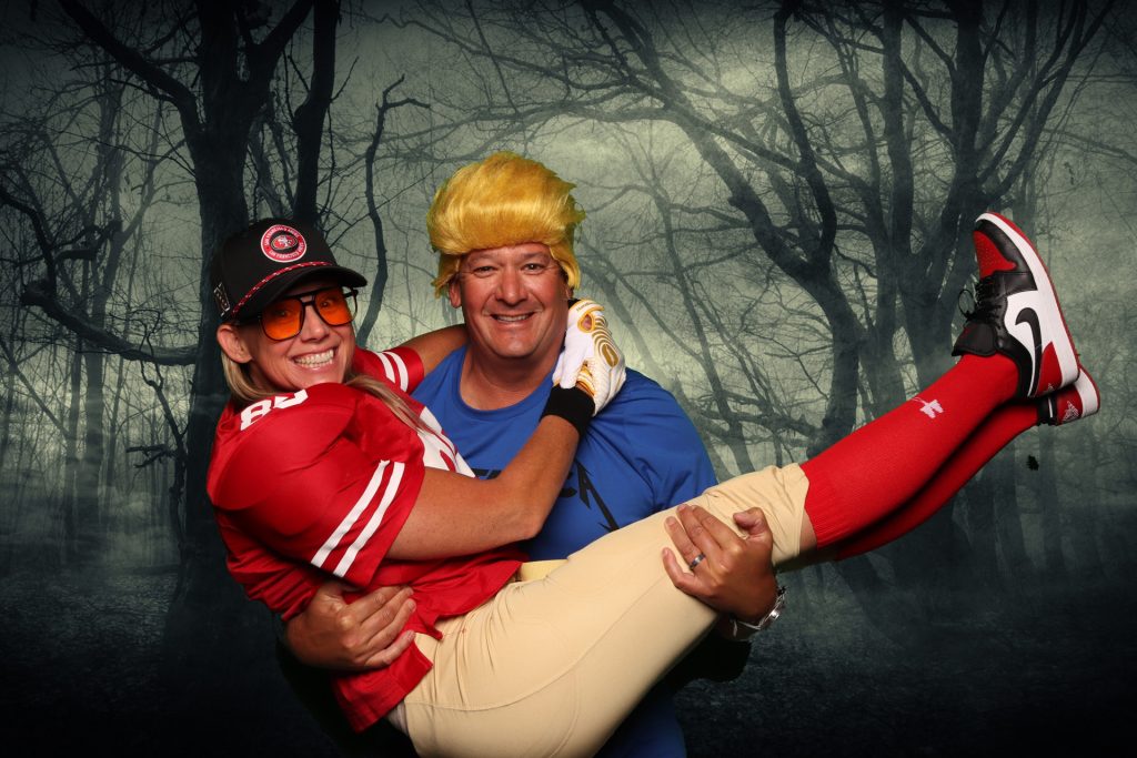 Man and woman dressed in costume taking a photo in front of a greenscreen Halloween Photo Booth.