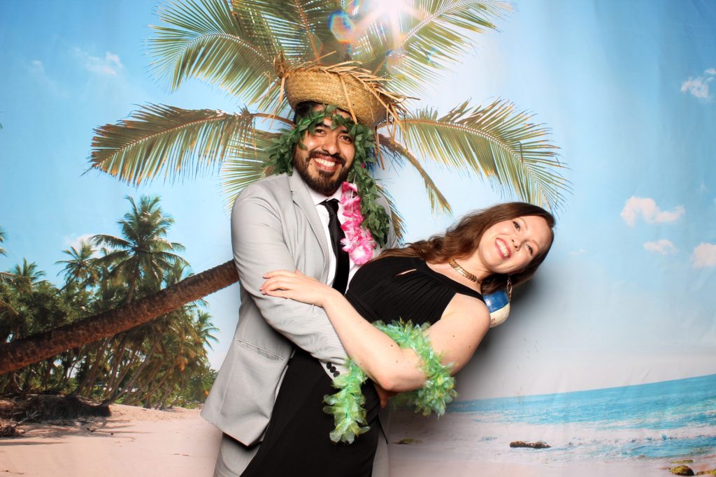 A couple poses for a photo in front of Beach backdrop.