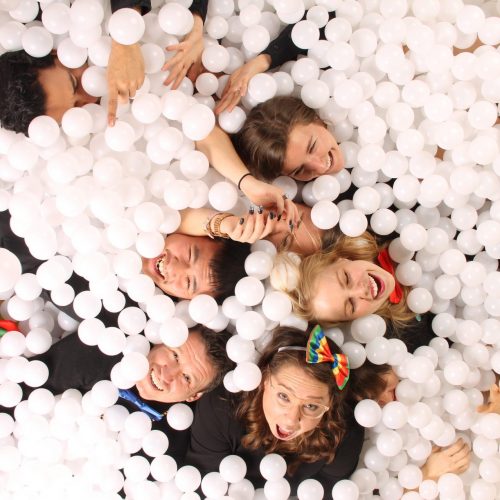 group of people having fun in a white ballpit photobooth