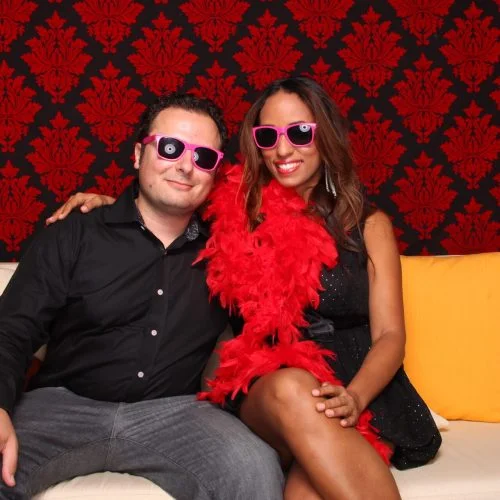 a man and a woman posing on a couch in front of a red and black background
