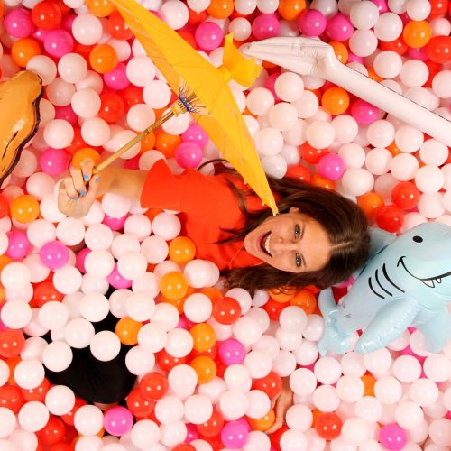 woman posing with a parasol in a white, pink, orange, and red ballpit photobooth