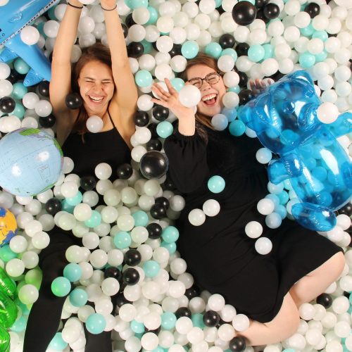 two women having fun in a blue, white, and black ballpit photobooth