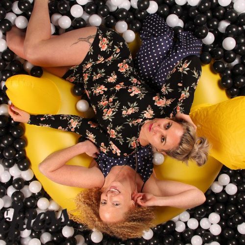 two women sitting on an innertube in a black and white ballpit photobooth