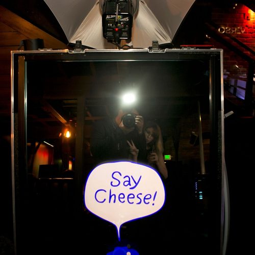 a photographer and a woman making a peace sign in a mirror photo booth