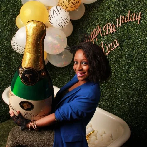 a woman sitting on a bathtub in a photobooth with a champagne balloon