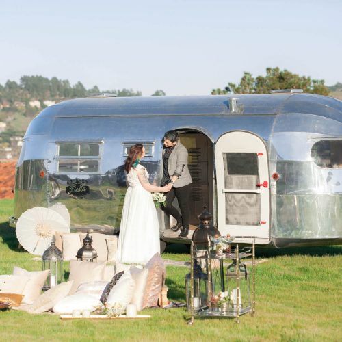 a bride and groom standing outside an airstream photo booth smiling at each other