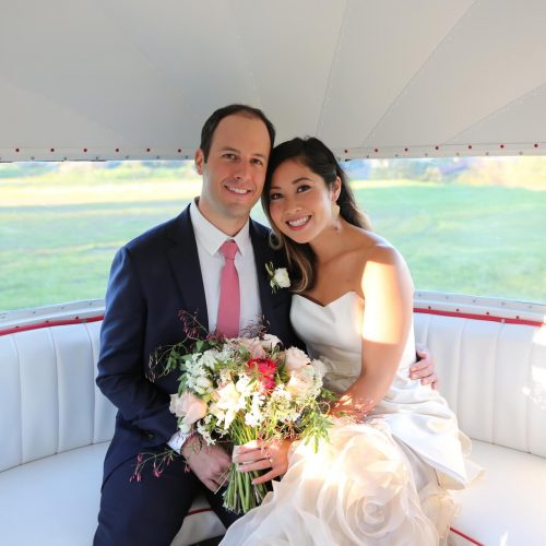 a couple sitting in an air stream photo booth at their wedding holding a bouquet