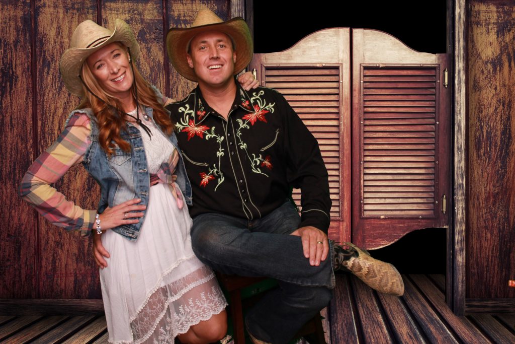 a man and a woman wearing cowboy hats in front of a saloon photo background