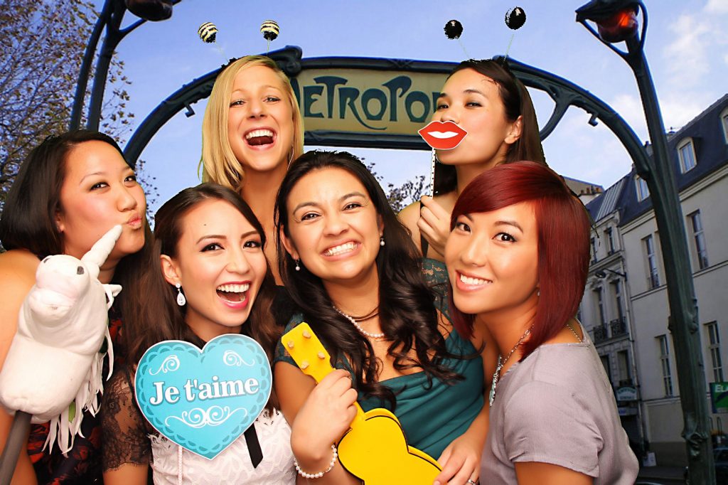 six women posing in a greenscreen photo booth with fun props