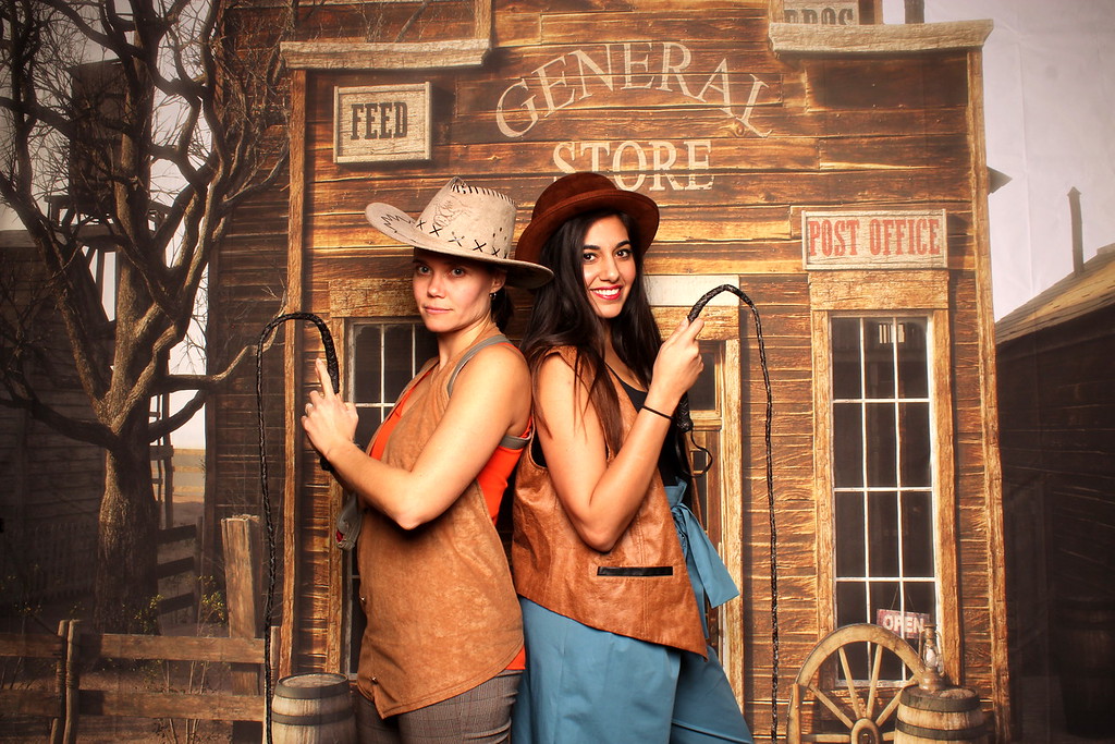 two women wearing Western attire and holding whips against a general store background