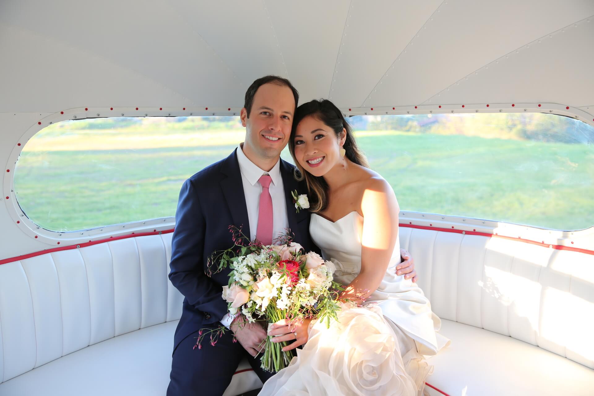 a couple sitting in an air stream photo booth at their wedding holding a bouquet